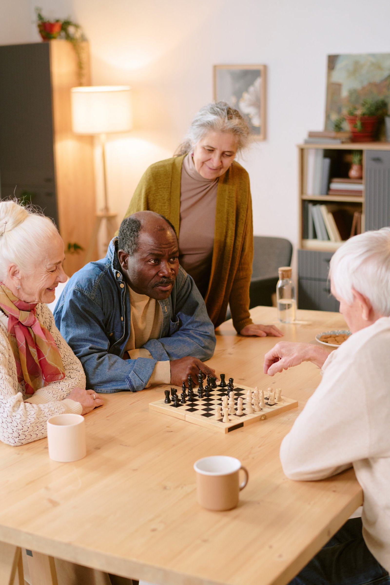 Vertical shot of biracial senior men sitting at table and playing chess while silver headed women watching them